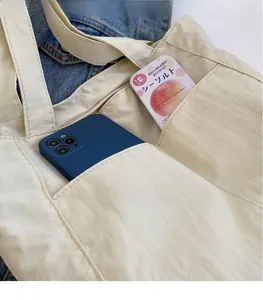 Detail of nylon tote bag showing multiple front pockets holding a phone and candies