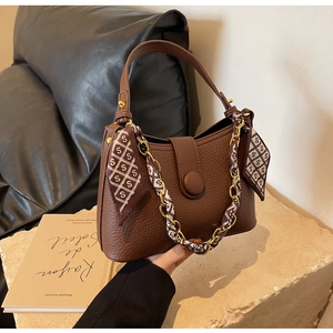Close-up of brown litchi pattern leather bag with chain and printed silk scarf