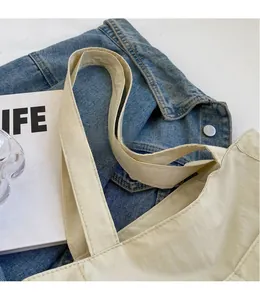 Detail of wide nylon shoulder strap and textured fabric on beige tote bag