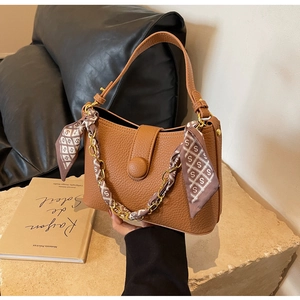 Detailed view of brown lychee leather bag featuring silk scarf wrapped around gold chain handle