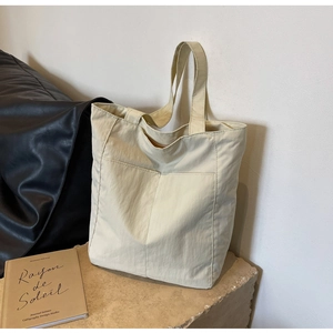 Minimalist cream nylon tote bag with front pocket shown in an elegant interior setting