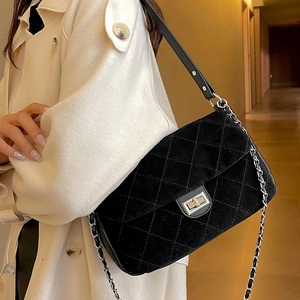 Quilted black suede chain shoulder bag with metal lock shown on model with beige coat