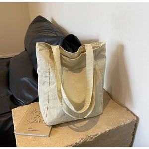Detail of cream nylon tote bag showing the front pocket and strap on a stone texture