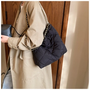 Détail d'un sac cabas noir matelassé avec bandoulière chaîne dorée porté à l'épaule