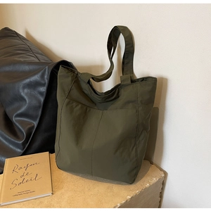 Detail view of the durable olive green nylon tote bag with vertical stitching on stone surface