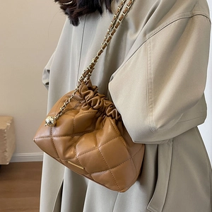 Brown quilted leather bucket bag with gold chain strap worn with a beige trench coat