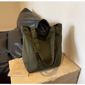 Detailed texture of olive green nylon tote bag on beige stone against black leather background
