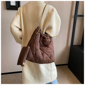 Détail du sac seau matelassé marron foncé avec chaîne dorée sur un manteau beige