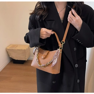Detail of brown litchi pattern leather bag with gold chain and silk scarf decoration