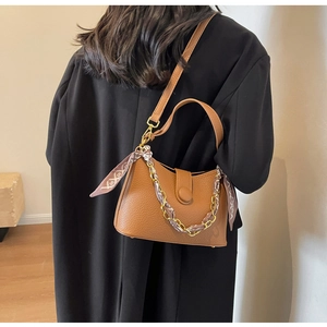 Macro detail of brown pebble leather handbag featuring a silk scarf wrapped metal chain
