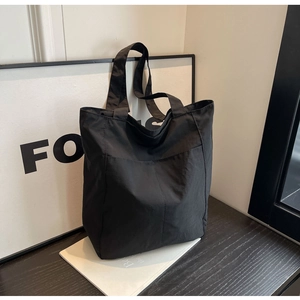 Macro detail of high-capacity black nylon tote bag with reinforced stitching and soft texture