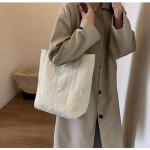 Detail of creamy white nylon tote bag showing pleated texture and large front pocket