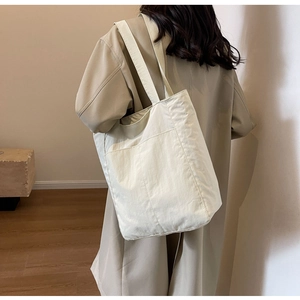 Detail of the cream nylon tote bag showing its large front pocket and lightweight texture