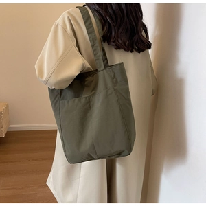 Deep olive green nylon tote bag detail showing large exterior pocket and fabric texture
