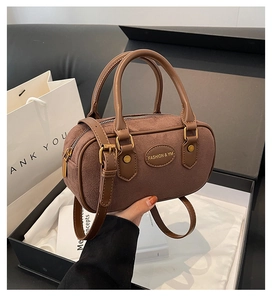 Detail of matte brown cylinder bag with retro bronze hardware and fashion logo