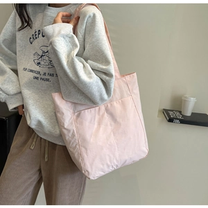 Detail of light pink nylon tote bag showing front pocket and minimalist shoulder strap design