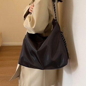 Large black Oxford cloth tote bag with woven rope shoulder strap worn with beige coat