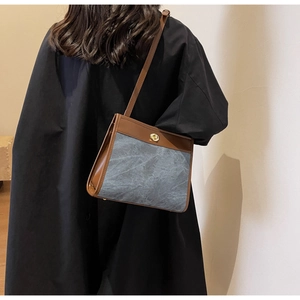 Detail of grey canvas and brown leather crossbody bag with golden metal twist lock