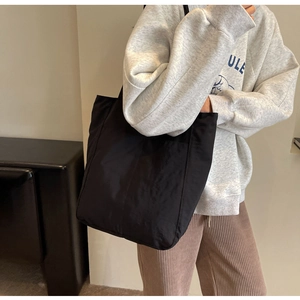 Side view of large black nylon tote bag worn by a model for a stylish minimalist look