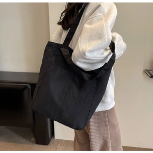 Close-up of black nylon tote bag with wide shoulder strap and large front pocket detail