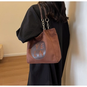 Détail du sac cabas en daim marron avec écusson YELN en cuir et bandoulière en chaîne