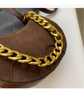 Detail of dark brown matte leather saddle bag with chunky gold chain decoration