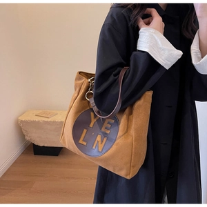 Détail d'un sac cabas en daim marron avec découpe YELN sur un manteau noir