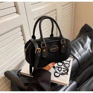 Close-up of black suede and leather boston bag featuring golden hardware and logo detail