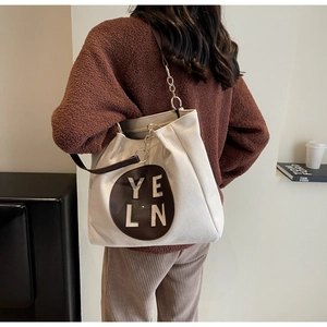 Détail du sac cabas en toile avec écusson en cuir et bandoulière chaîne porté par un mannequin