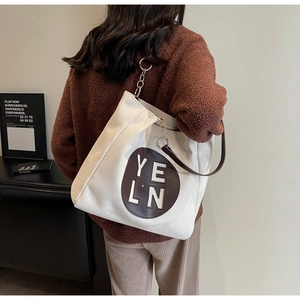 Détail d'un grand sac fourre-tout beige avec bandoulière en cuir marron et logo YELN