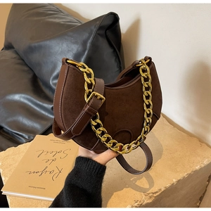 Detail of dark brown suede saddle bag with chunky gold chain on stone surface