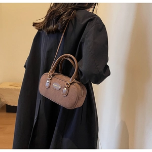 Detailed side view of a brown vintage matte cylinder bag held by a model in black coat