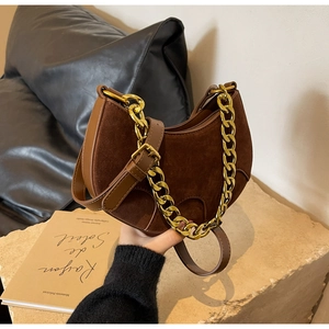 Detail of brown suede crescent bag with gold chain and leather strap on a textured surface