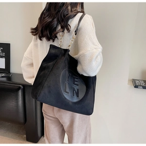 Détail du sac fourre-tout noir mat avec chaîne dorée et écusson design sur suédine