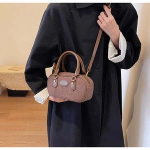 Close-up of a brown suede Boston bag with leather handles shown in a lifestyle setting