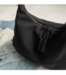 Detail of black nylon crescent bag featuring dual zippers and woven pulls in a minimal style