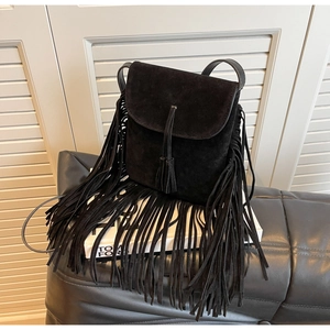 Gros plan sur un sac bandoulière noir mat avec de longues franges bohèmes sur bois