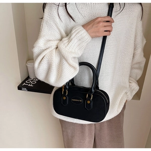 Detail of black frosted boston bag with fashion tag held by model in knit sweater