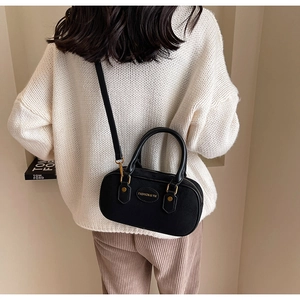Detailed view of the black cylindrical vintage crossbody bag worn by a model in a sweater