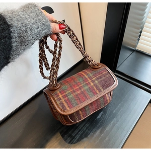 Detail of red and green plaid crossbody bag with metal chain strap and leather trim