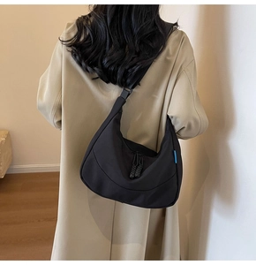 Detail of a large black nylon crescent bag featuring a woven zipper pull and blue side tag