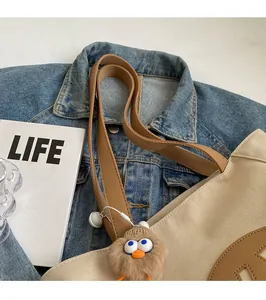 Detail of beige canvas tote bag with brown leather straps and plush bird pendant