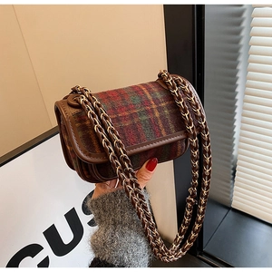 Detail of red and green plaid crossbody bag featuring leather woven chain strap and flap