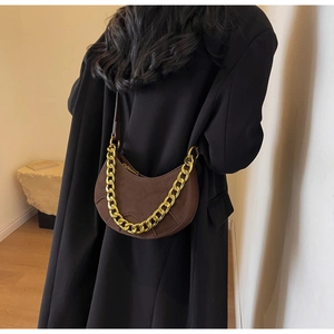 Detail of a brown suede half-moon saddle bag with a chunky gold chain strap on a black coat