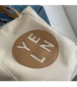 Detail of off-white nylon tote bag with brown leather patch and YLNE cutout design
