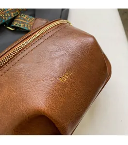 Close-up of brown pebbled leather chest bag with gold zipper and patterned strap