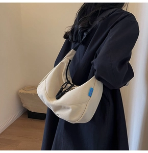 Detail of off-white crescent crossbody bag with black braided rope and blue woven label