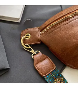 Detail of brown textured leather bag with gold hardware and geometric woven strap