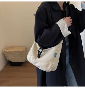 Close-up of cream nylon dumpling bag with black woven drawstring and blue side label