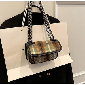 Detail of green plaid crossbody bag featuring woven chain strap and leather trim accents